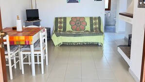 Een gezellige woonkamer met houten plafond, een bank met decoratief plaid, een eettafel met stoelen en een televisie.