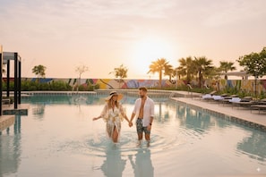 A couple holding hands in a swimming pool with a colorful mural in the background.