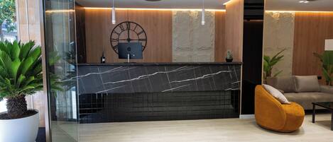A modern reception area with a marble counter, a large clock, and a comfortable seating area with a yellow chair.