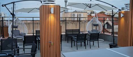 An outdoor seating area with tables and chairs, a wooden partition, and hanging chairs.