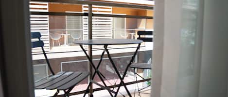 Ein Balkon mit Tisch und Stühlen, Blick auf die Außenansicht des Gebäudes und ein Fenster mit Jalousien.