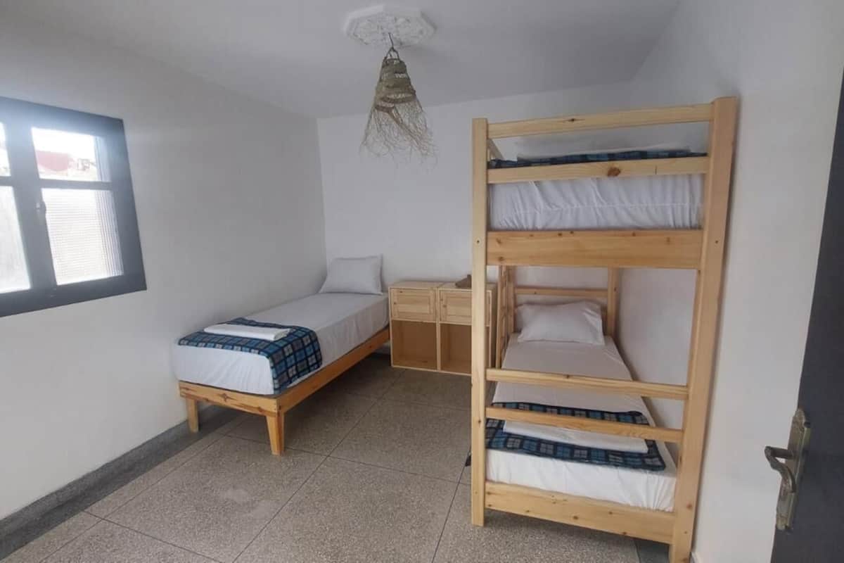 A dormitory room with bunk beds, a single bed, a small desk, and a window.