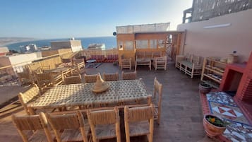 Terraço no telhado com mobiliário de vime, piso de azulejos e vista para o mar.