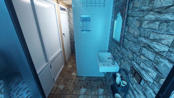 Un couloir étroit avec une porte blanche, un mur en pierre et un petit lavabo avec un robinet.