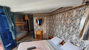 A hotel room with a bunk bed, a heart-shaped mirror, patterned wallpaper, and a small wooden side table. - HABIBI HOSTEL (Taghazout)