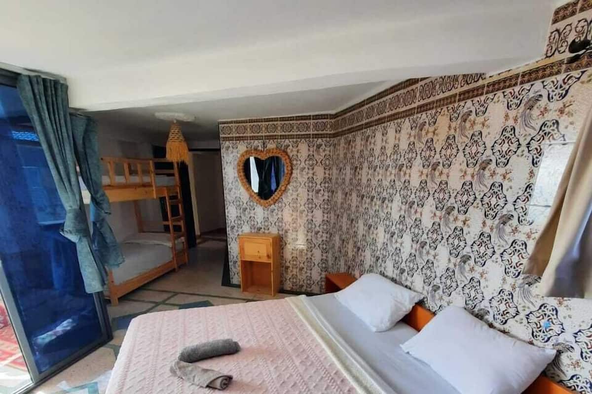 A hotel room with a bunk bed, a heart-shaped mirror, patterned wallpaper, and a small wooden side table.
