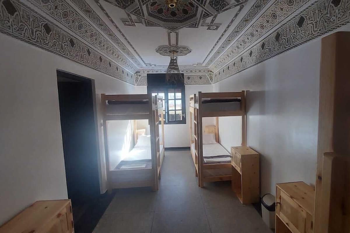 A room with bunk beds, a ceiling with intricate patterns, and a window allowing natural light.