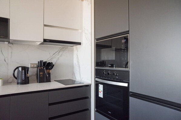 Private kitchen with a marble-look backsplash, induction cooktop, built-in oven, microwave, and sleek dark cabinetry. - Bright Apartment in Prime Nunoa: Gym and Balcony (Unknown)