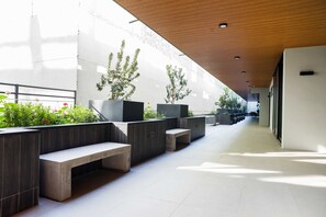 Un espacio interior moderno con un largo pasillo, bancos y macetas con plantas.