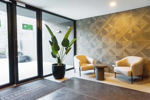 Un lobby moderno con una planta en maceta, dos sillones, una mesita redonda y una pared con estampado geométrico.