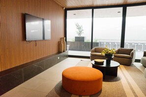 A modern living room with a flat-screen TV mounted on the wall, a round orange ottoman, two sofas, and a coffee table with a plant. - Central Apartment with Balcony and Free Parking (Unknown)