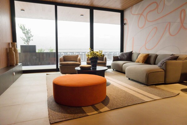 Una sala de estar moderna con sofá, reposapiés y mesa de centro, ventanas amplias con vistas, y jarrones decorativos.