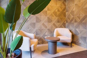 A modern lounge area with two armchairs and a round table, a large potted plant, and a geometric patterned wall.