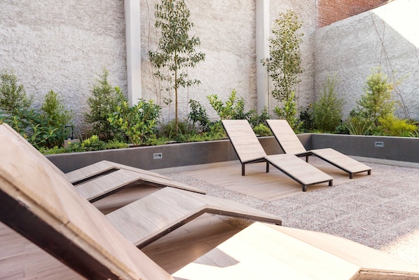 Una terraza en la azotea con sillones de madera, una jardinera de hormigón con plantas y una pared con textura.