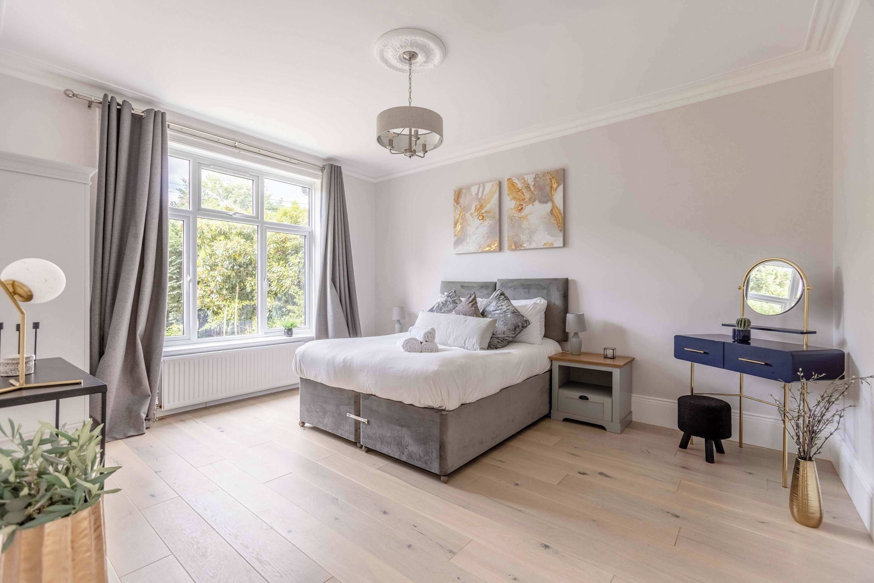 A bedroom with a bed, bedside tables, a dresser, a mirror, and artwork on the wall.