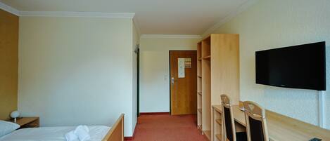 A hotel room with two beds, a desk, chairs, a TV, and a wooden wardrobe.