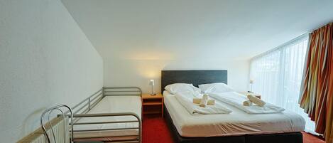 A hotel room with a single bed, a chair, a small table, and a radiator.