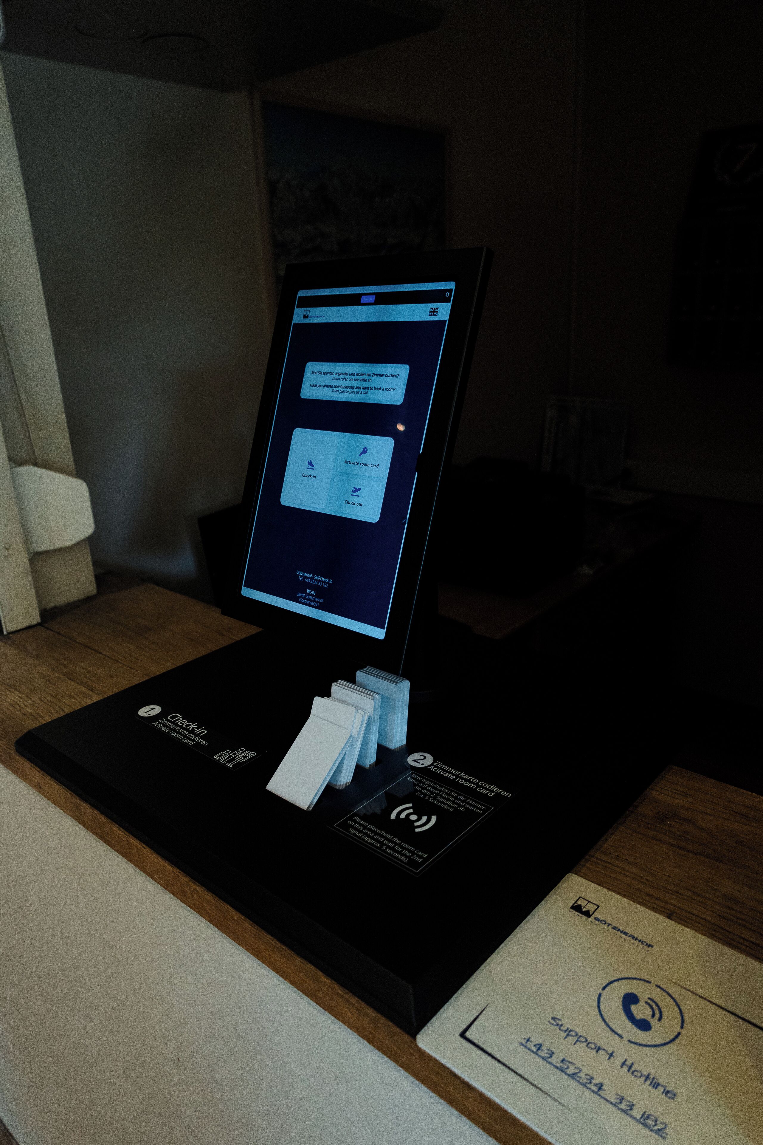 Un chiosco digitale con un cartello per l'assistenza telefonica, un lettore di carte e uno schermo che mostra un messaggio.