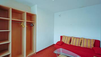 Una habitación con un sofá rojo, una mesa de centro de cristal y un armario de madera con varios estantes.