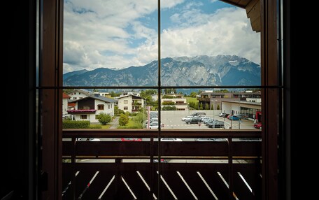 A view through a window with a wooden frame, overlooking a parking lot and buildings, with mountains in the background.
