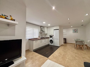 A modern kitchen with a washing machine, a dining area with a table and chairs, and a TV on a stand.