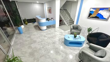 Un espace d’accueil avec un bureau bleu et blanc, un fauteuil gris, une table basse bleue et un escalier en arrière-plan.