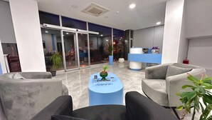 Una hall moderna con reception, area salotto e porte in vetro che conducono in un'altra stanza.