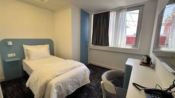 A hotel room with a single bed, a desk with a telephone, and a window with curtains.