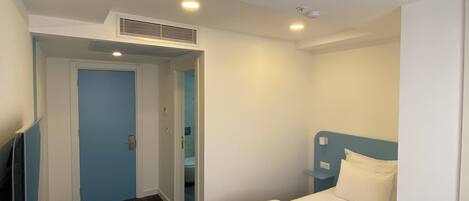 A hotel room with a bed, a desk with a computer, a chair, and a bathroom visible through an open door.