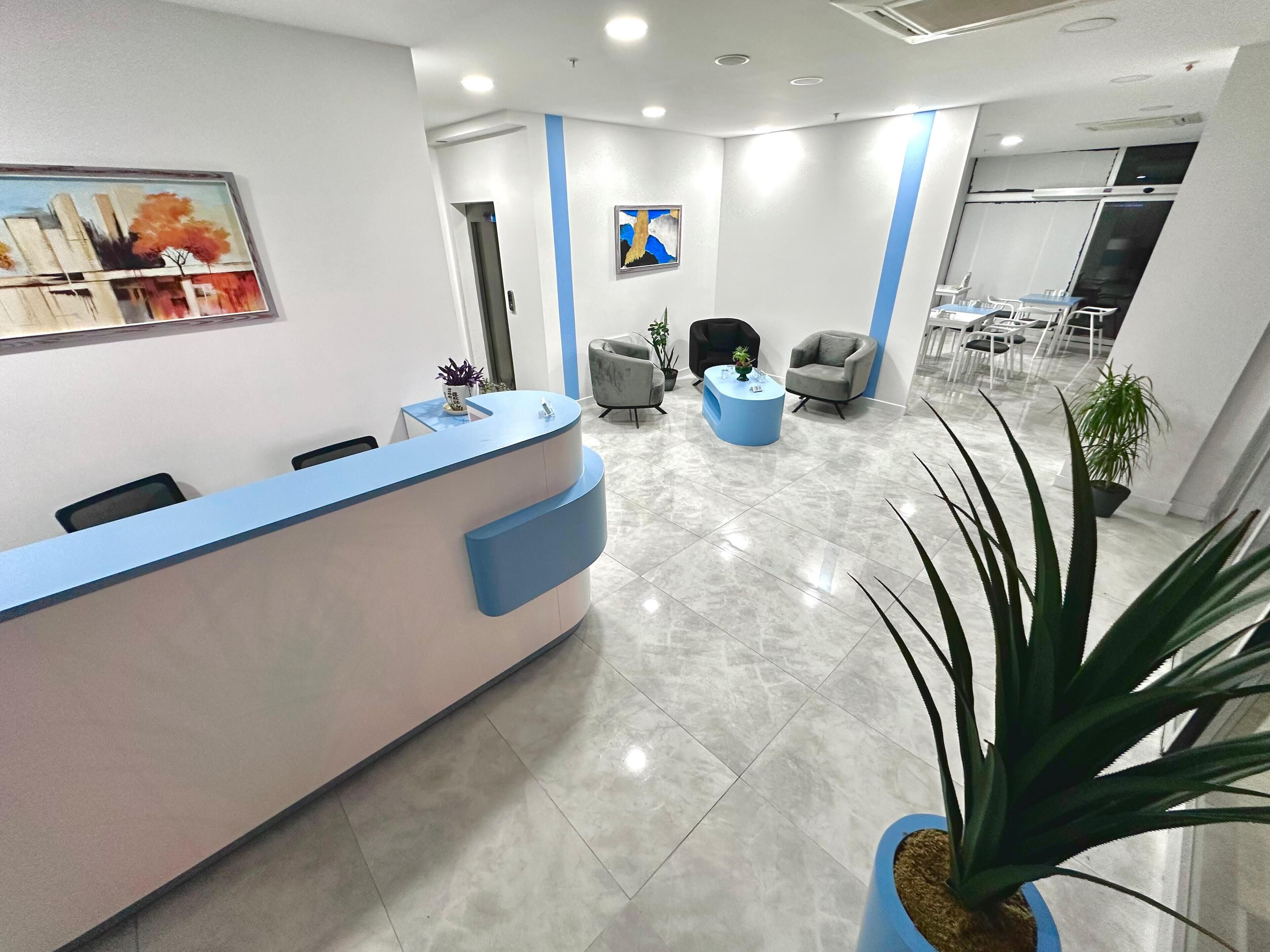 A reception area with a blue counter, several chairs, and potted plants.