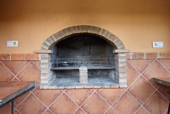 A brick oven fireplace with a tiled wall and a small table to its left.