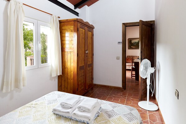 A bedroom with a bed, a wooden wardrobe, a fan, and a view through an open door.