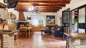 A rustic interior with a wooden ceiling, a dining area with a table and chairs, a sofa, and a kitchen area with cabinets and a stove.