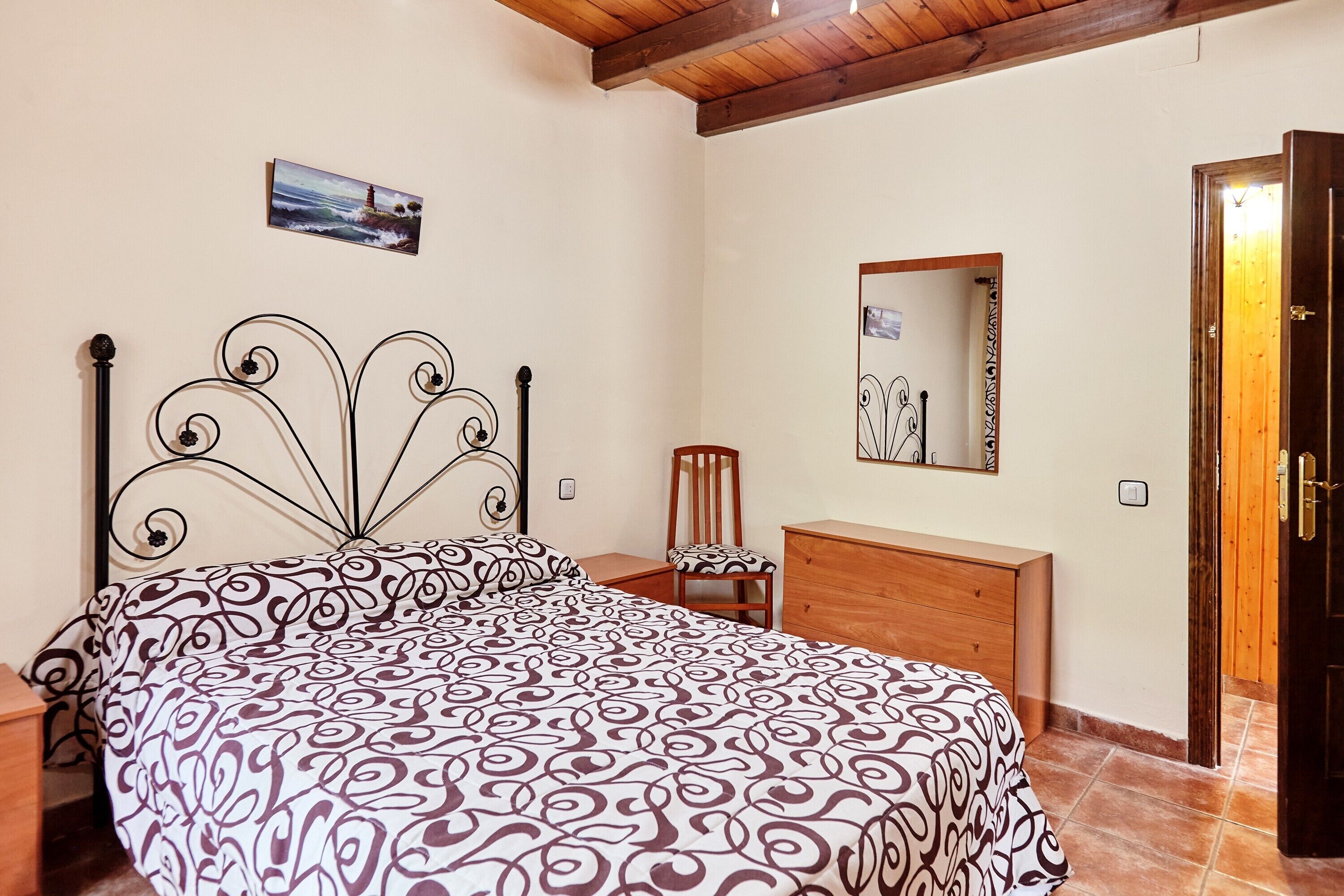Un dormitorio con una cama, un aparador de madera, una silla, un espejo y una puerta.