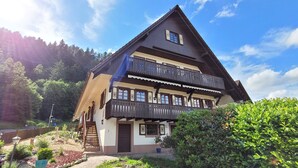 Ein traditionelles Chalet mit Balkon, einer Holztreppe und einem Garten.