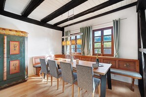 A dining area with a wooden table, four chairs, a bench, a cabinet with floral designs, and a window with curtains.