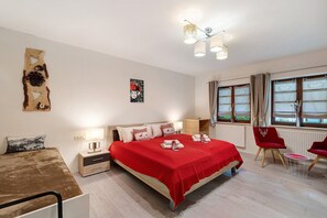 A bedroom with a bed, bedside tables, a chair, a small table, and a window with curtains.