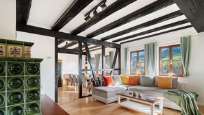Ein geräumiges Wohnzimmer mit freiliegenden Holzbalken, einer Couch mit bunten Kissen und einem grünen Schrank.