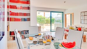 Un salon moderne comprenant un coin repas, une grande bibliothèque remplie de livres et une vue sur une piscine et la verdure environnante.