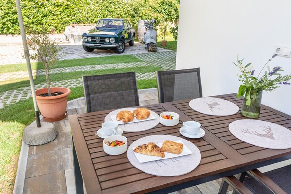 A patio table with plates of food, a potted plant, and a vintage car in the background. - Holiday Apartment Berta – new, comfortable, with garden terrace & mountain view (Sankt Martin in Passeier)