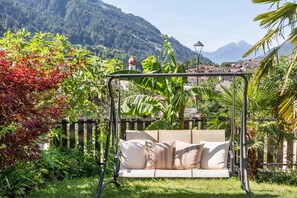 Un jardín con una silla hamaca, abundante vegetación y montañas al fondo.