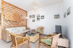 A room with a sofa, two wicker chairs, a small table, a TV, and wall art. - Holiday Home 'On The Sea Fenicottero' with Sea View, Private Terrace and Private Garden (S'Ena e Sa Chitta)
