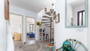 A hallway with a spiral staircase, a mirror, a wicker chair, and a glass table with a decorative bowl. - Holiday Home 'On The Sea Fenicottero' with Sea View, Private Terrace and Private Garden (S'Ena e Sa Chitta)