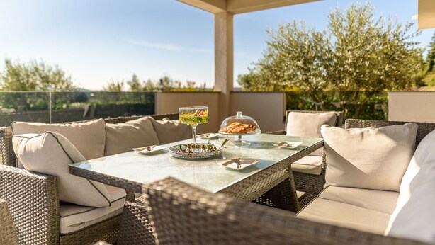 Een terras buiten met rieten meubels, een glazen tafel en een schaal eten.