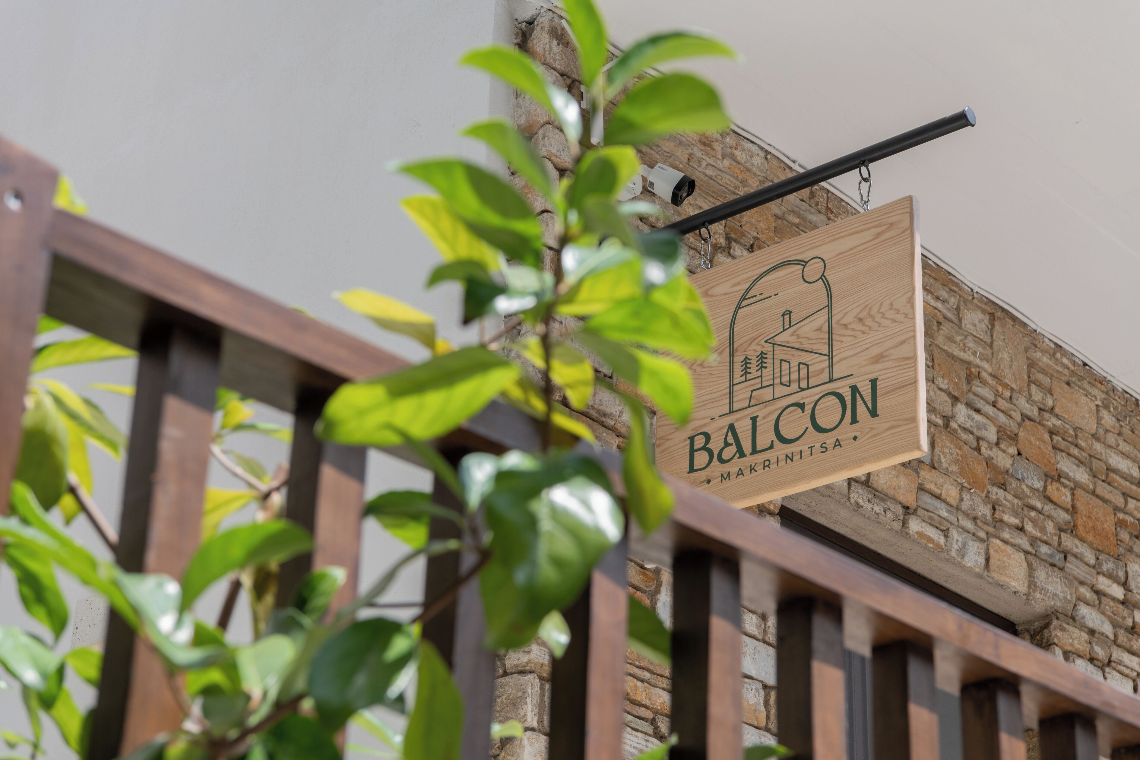 Un letrero de madera con el texto "BALCON" y "MAKRINTSA" sobre una pared de piedra.