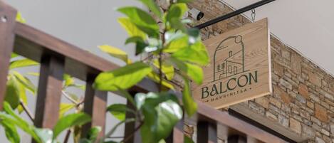 Un letrero de madera con el texto "BALCON" y "MAKRINTSA" sobre una pared de piedra.