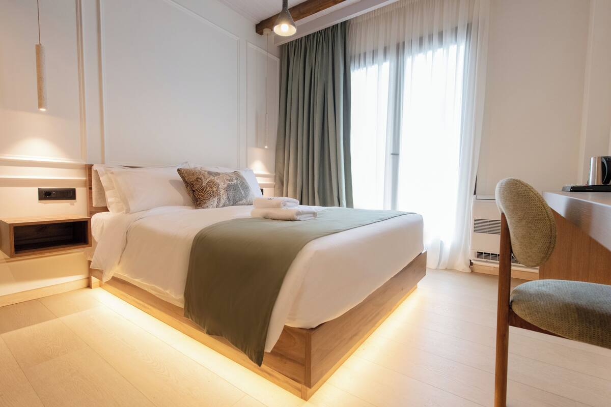 A modern bedroom with a wooden bed, a bedside table, a chair, and a large window with curtains.