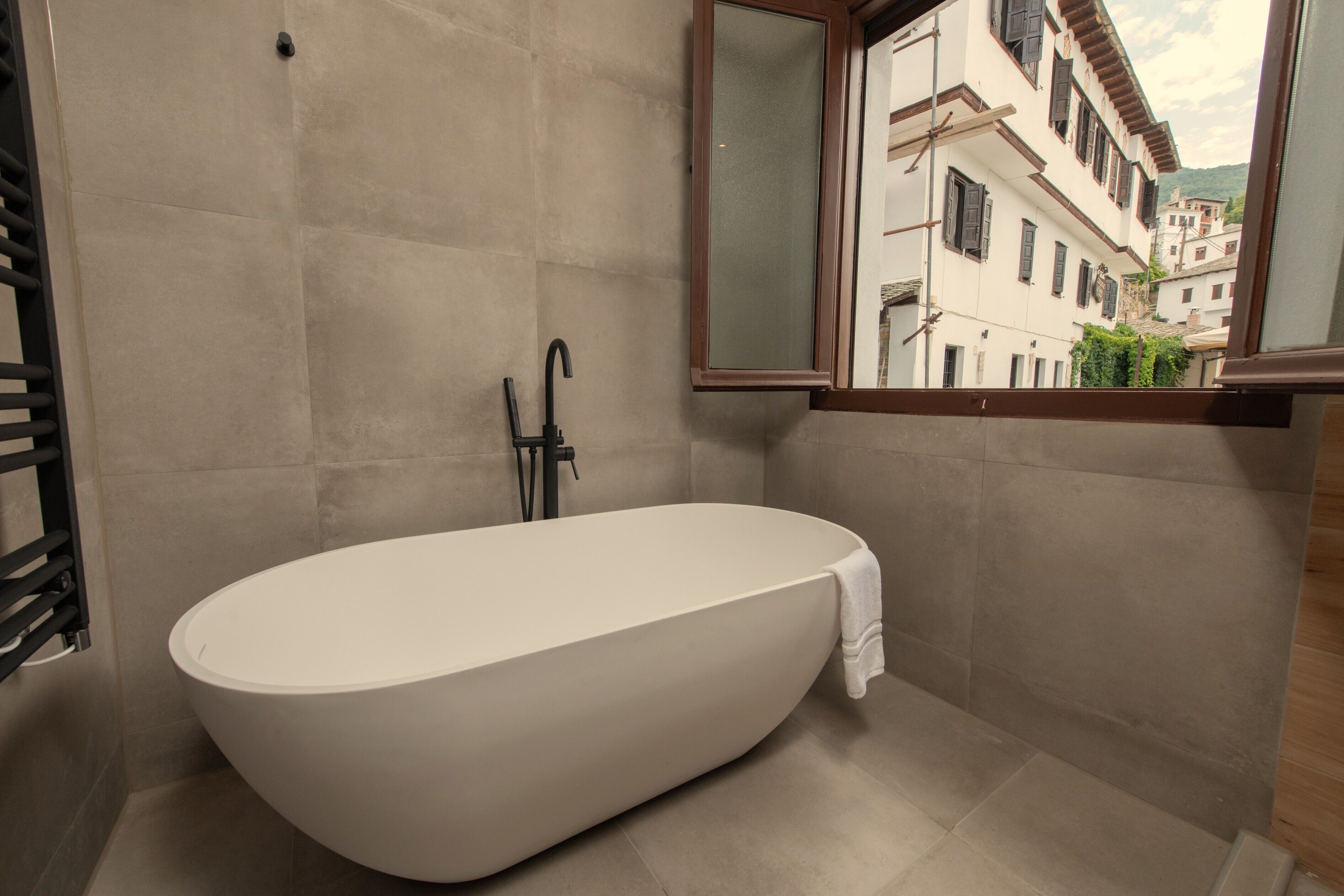 Un baño moderno con una bañera independiente, un ventanal con vistas a edificios y un perchero para toallas.