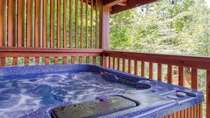 Een hottub met een blauwe mozaïekrand, een houten terras en uitzicht op een bebost gebied.