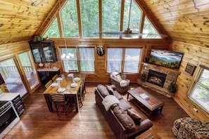 Un intérieur de chalet chaleureux comprenant un coin repas, une cheminée, un canapé et un téléviseur.